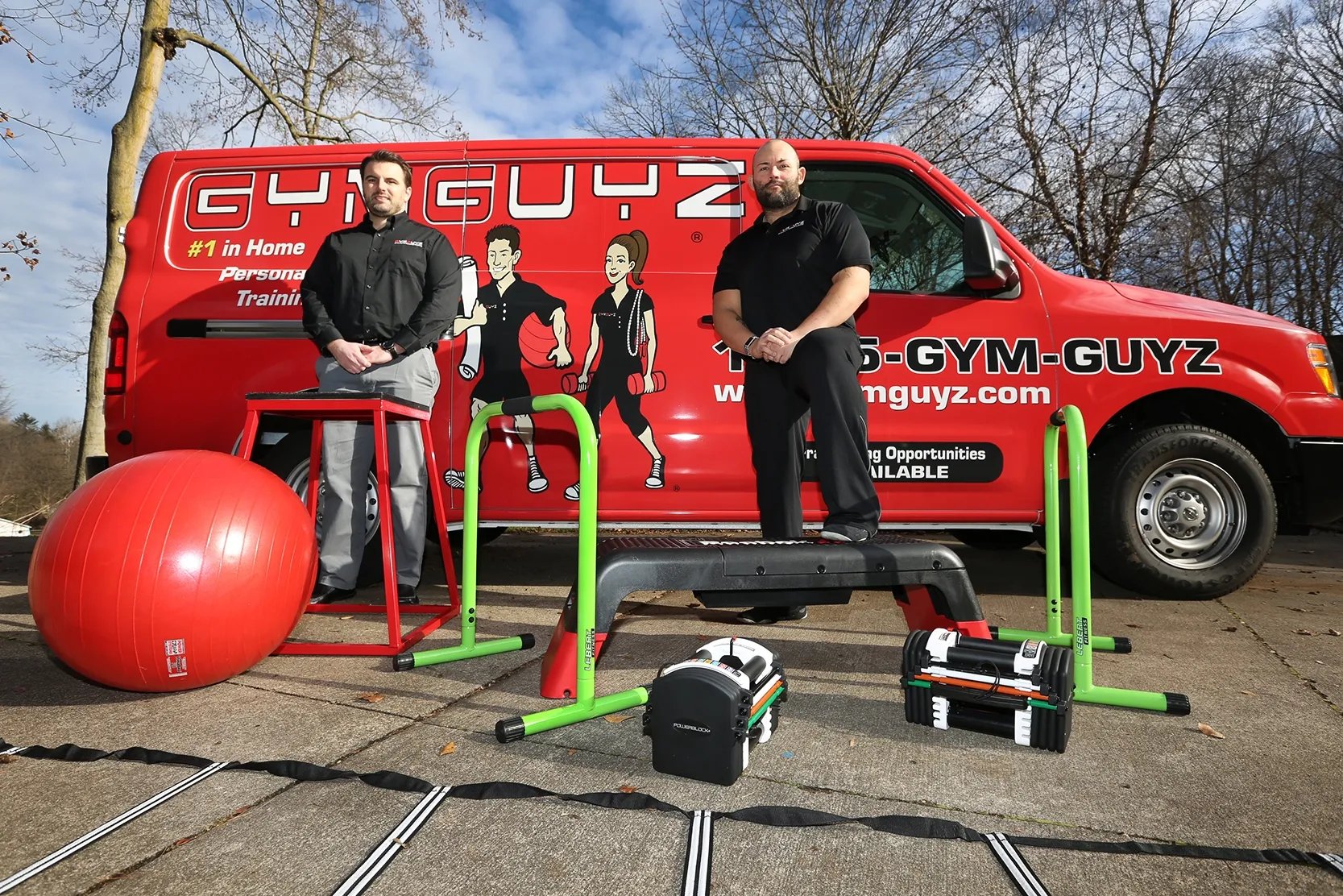 Trainers standing beside a GYMGUYZ van with the equipment used in the classes.