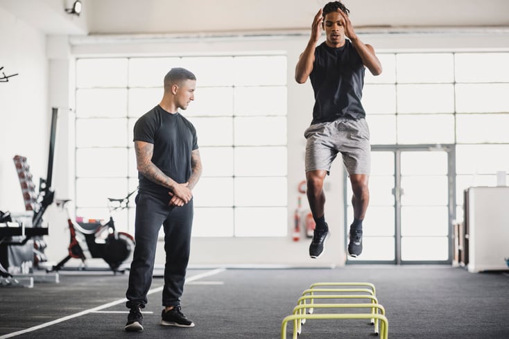 A CrossFit trainer helping a CrossFitter in a CrossFit box through a WOD