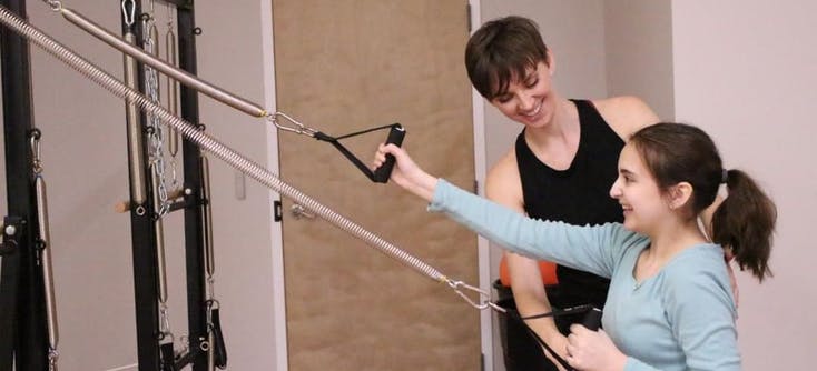 An instructor helping someone learn to teach Pilates in a Pilates studio