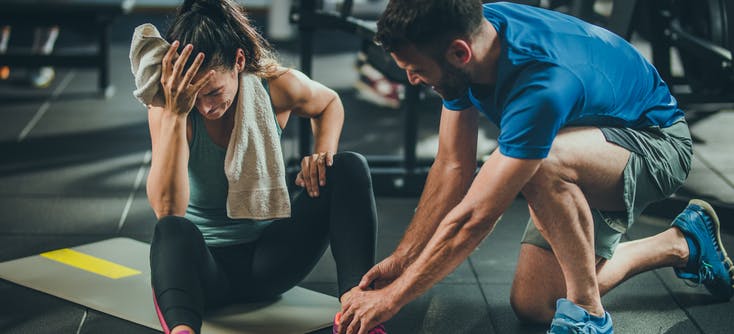 A fitness instructor helps an injured client in a gym.