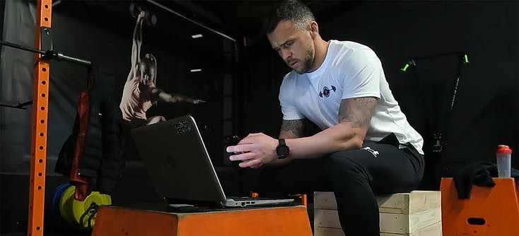A personal trainer checking his social media on his phone and laptop in his fitness studio.