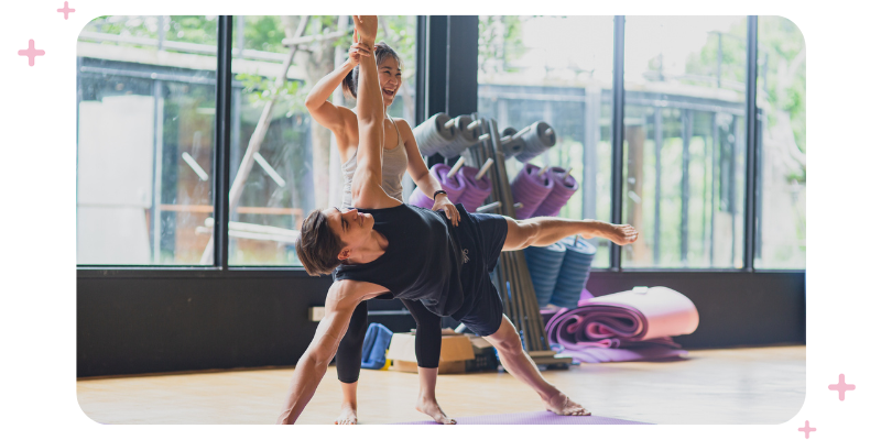 A yoga teacher helps a yogi perform a yoga pose during a yoga class