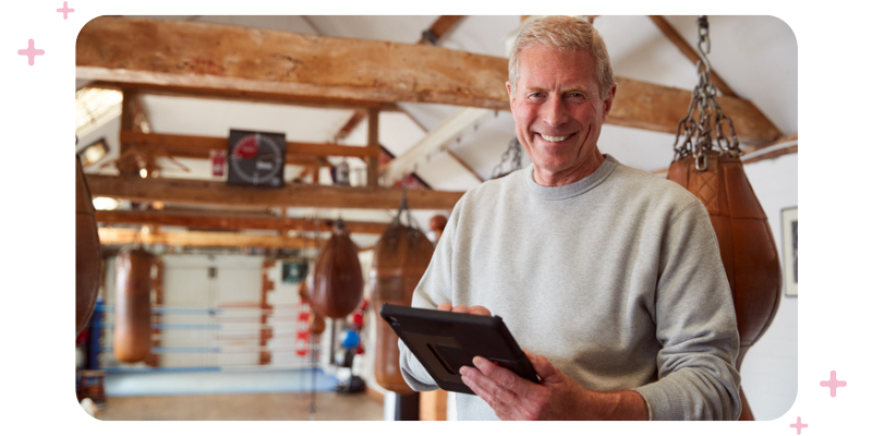 A boxing gym owner holding a clipboard, standing in front of punching bags.