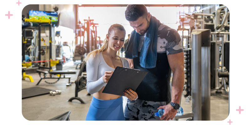A personal trainer getting ready to start a fitness assessment with her client at the gym; both people are in workout clothes.