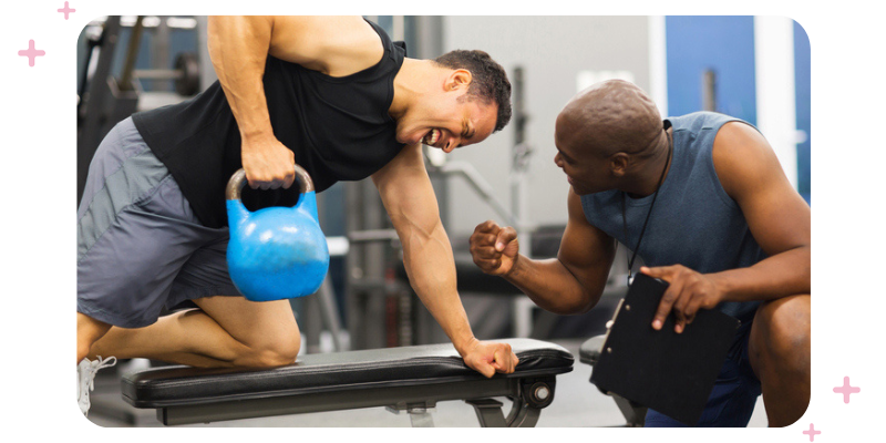 A coach motivating his client as the client lifts a heavy kettlebell.