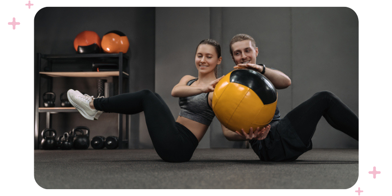 Couple passing a medicine ball to each other during a workout at the gym.