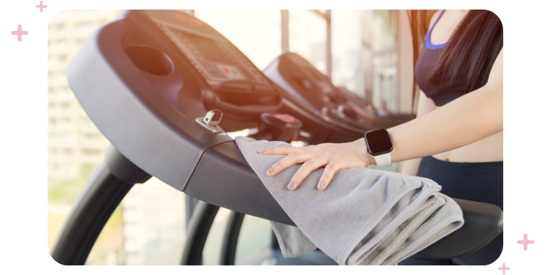 A gym customer wiping down a running machine after using it.