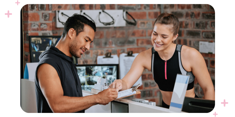 Man signing up at a gym, with a female employee helping him at the reception desk.