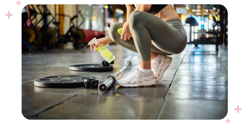 Woman in workout gear cleaning equipment at the gym.