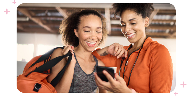 Two women at the gym looking at a mobile phone and smiling.